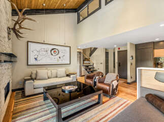 Experience luxury mountain living in this stunning great room, featuring a soaring vaulted ceiling with exposed wood beams and a dramatic stone fireplace adorned with impressive antlers.