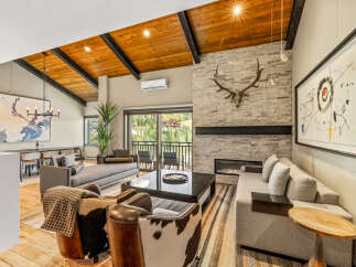 Experience luxury mountain living in this stunning great room, featuring a vaulted wood-beamed ceiling and a striking stone fireplace.
