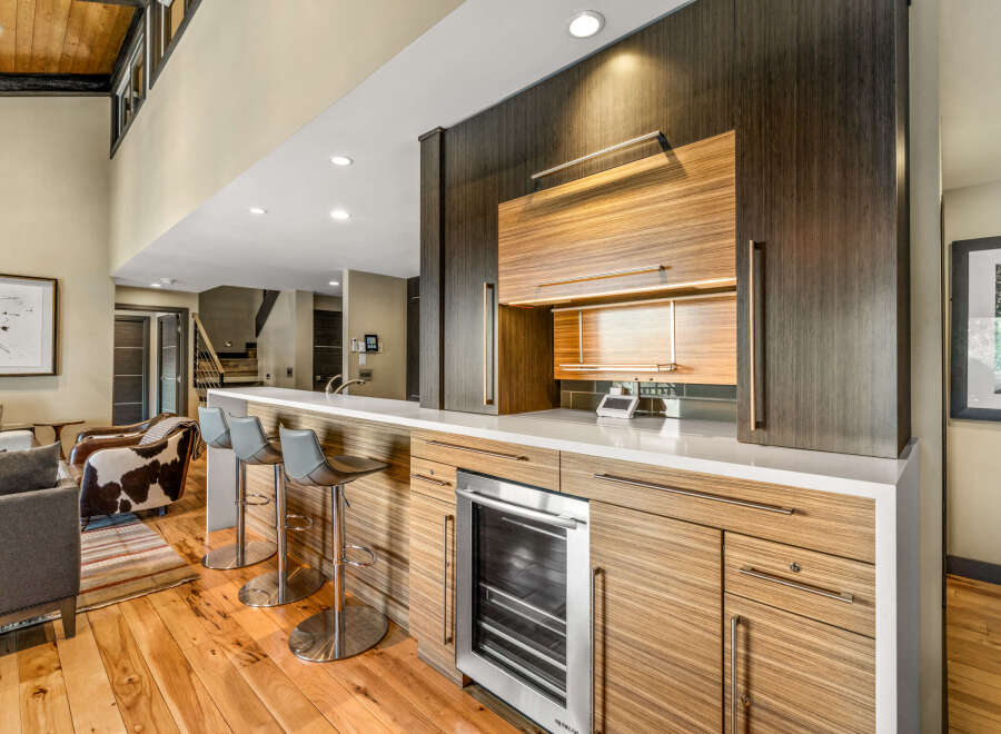 Experience luxury living with this stunning modern wet bar, featuring sleek cabinetry and a built-in wine cooler.