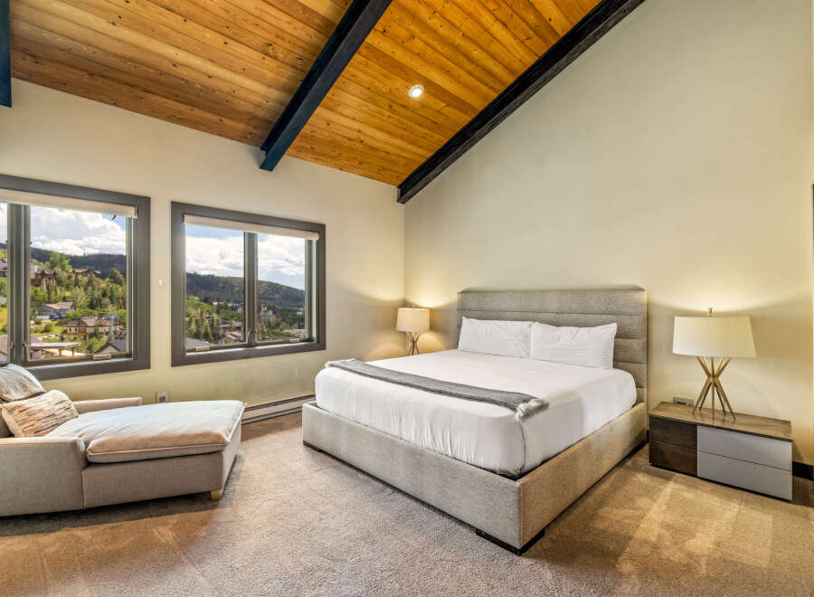 Experience luxury mountain living in this stunning bedroom, featuring a spacious king-sized bed and a comfortable chaise lounge.