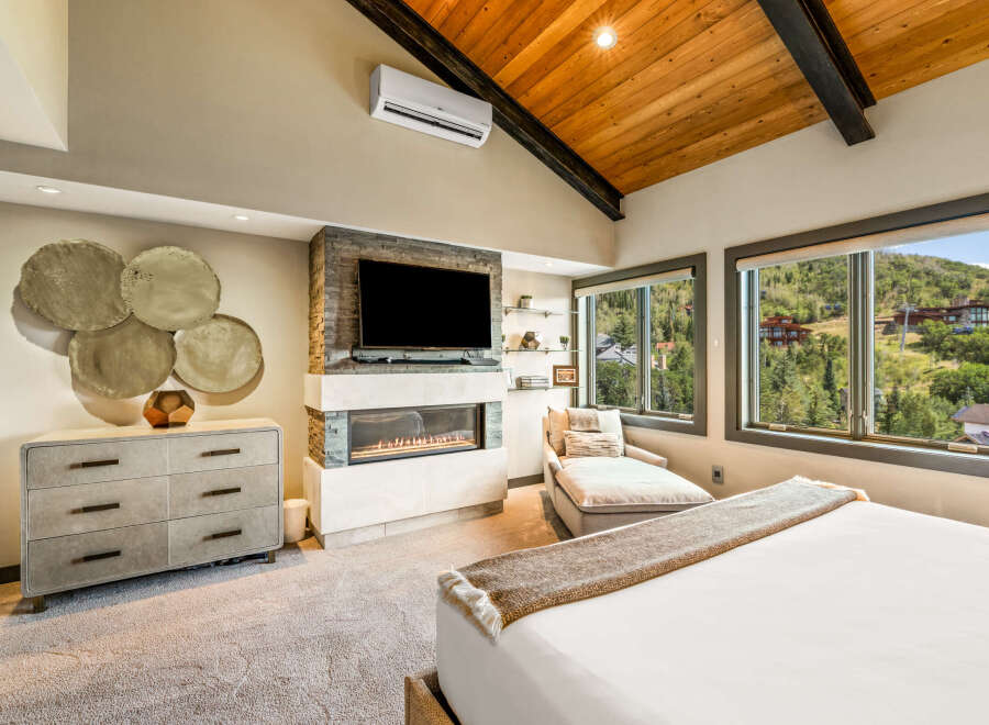 Experience luxury mountain living in this stunning bedroom featuring a modern gas fireplace and a large flat-screen TV.