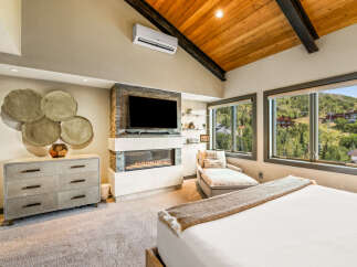 Experience luxury mountain living in this stunning bedroom featuring a modern gas fireplace and a large flat-screen TV.