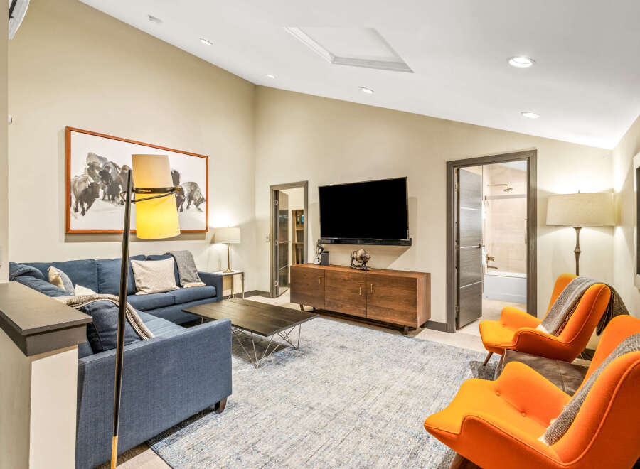 Experience modern comfort in this stylish living room, featuring a deep blue sectional sofa complemented by vibrant orange accent chairs.