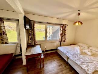 This charming hotel room offers a comfortable double bed, a functional desk area with a TV, and large windows with scenic views of the surrounding landscape.