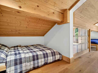 Experience cozy living in this charming attic bedroom, featuring a plaid-covered bed nestled under exposed wooden beams.
