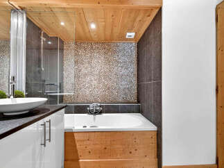 Experience rustic charm in this bathroom featuring a unique pebble tile accent wall and a wooden bathtub surround.