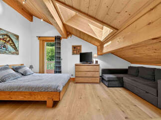 Experience cozy mountain living in this charming attic bedroom, featuring a comfortable wooden bed and a spacious sectional sofa perfect for relaxation.