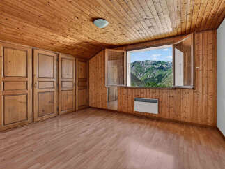 Experience breathtaking mountain views from this charming room, featuring a sloped wooden ceiling and walls that create a cozy, rustic ambiance.