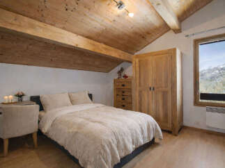 Experience cozy mountain living in this charming attic bedroom, featuring a plush bed, a rustic wooden wardrobe, and a convenient desk area.