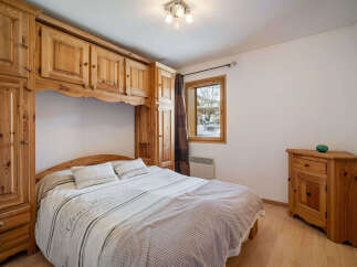 This charming bedroom features a cozy bed with a decorative duvet and pillows, complemented by a large wooden wardrobe and overhead cabinets providing ample storage.