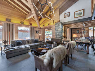 Experience luxurious mountain living in this stunning chalet, featuring a grand living area with a stone fireplace and exposed wooden beams.