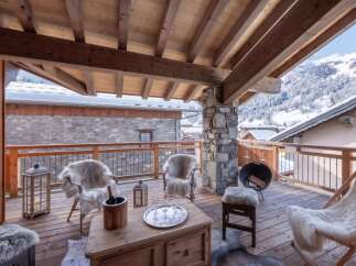 Experience ultimate relaxation on this stunning wooden balcony, complete with plush, fur-covered seating and a cozy fire pit, perfect for enjoying the breathtaking mountain views.