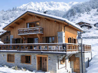 Experience luxury mountain living in this stunning chalet, featuring warm wooden exteriors and stone accents, perfect for a snowy getaway.