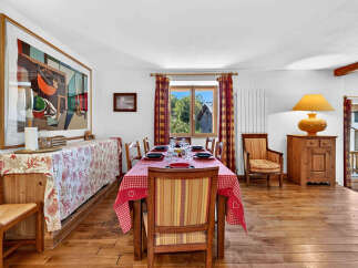 This charming dining room features a large, rustic wooden table set for a meal, adorned with a red and white checkered tablecloth.