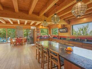 Experience rustic charm in this spacious log cabin kitchen, featuring a large granite island perfect for gatherings and a cozy dining area with a view of the lush outdoors.