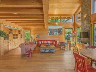 Experience luxurious living in this stunning wooden home, featuring an open-concept living area with a cozy fireplace and ample natural light.