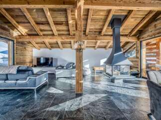 Experience luxurious mountain living in this stunning chalet featuring a rustic wooden beam ceiling and a modern, sleek fireplace.