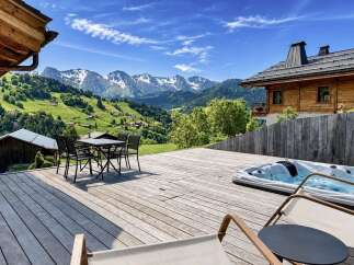 Experience breathtaking mountain views from this stunning chalet's expansive wooden deck, complete with a luxurious hot tub and outdoor dining area.