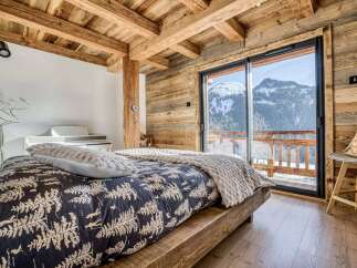 Experience luxury mountain living in this stunning bedroom featuring a rustic wooden ceiling and walls, complemented by a cozy bed with a nature-inspired duvet.