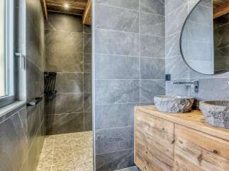 Experience rustic luxury in this stunning bathroom, featuring a spacious walk-in shower with pebble flooring and elegant grey stone tiles.
