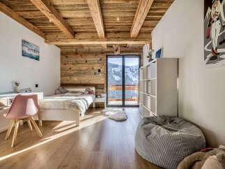 Experience cozy mountain living in this charming bedroom featuring rustic wooden beams and walls, complemented by a plush white bed and a modern desk area.