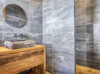 Experience rustic luxury in this stunning bathroom, featuring a unique stone vessel sink atop a warm, wooden vanity.