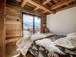 Experience cozy mountain living in this charming bedroom featuring rustic wooden walls and a vaulted ceiling with exposed beams.
