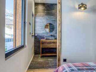 Experience rustic charm in this mountain retreat, featuring exposed wooden beams and a modern bathroom with a stone sink and tiled walls.