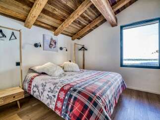 Experience cozy mountain living in this charming bedroom featuring a rustic wooden ceiling with exposed beams and a comfortable bed adorned with festive bedding.