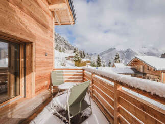 Experience breathtaking mountain views from this charming wooden balcony, perfect for enjoying a snowy landscape.