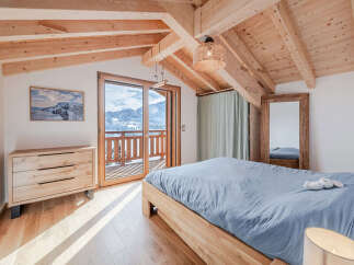 Experience cozy mountain living in this charming bedroom featuring a wooden-beamed vaulted ceiling and a private balcony with stunning snowy vistas.