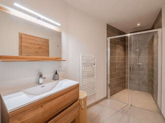 Experience modern luxury in this stunning bathroom featuring a sleek vanity with a wooden cabinet and a spacious walk-in shower with elegant tilework.