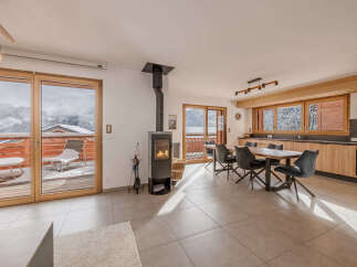 Experience cozy mountain living in this stunning open-plan living space, featuring a modern wood-burning stove and a spacious dining area perfect for gatherings.