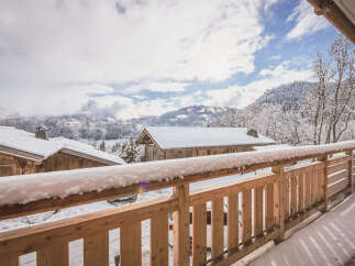 Experience the charm of a winter wonderland from this stunning balcony, offering breathtaking views of snow-covered mountains and traditional wooden chalets.