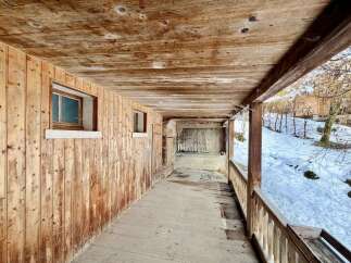 Experience rustic charm with this wooden-clad property, featuring a covered porch overlooking a serene, snow-dusted landscape.