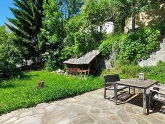 Enjoy outdoor living in this charming backyard featuring a rustic wooden table and chairs set on a stone patio.