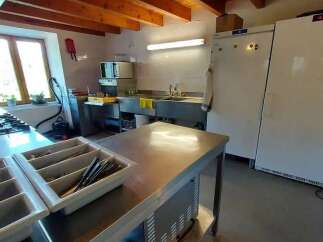 This spacious commercial kitchen features a large stainless steel prep table, a double sink, and ample storage with two full-size refrigerators.