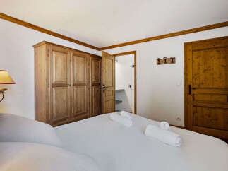 This charming bedroom features a large wooden wardrobe and a comfortable bed adorned with neatly folded towels.