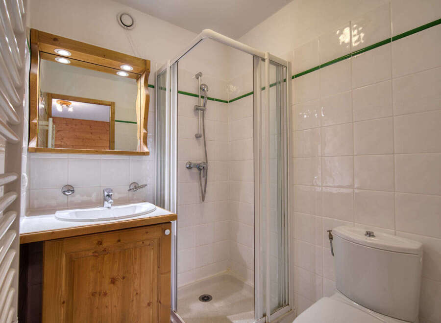 This charming bathroom features a wooden vanity with a white sink and a large mirror with built-in lighting.