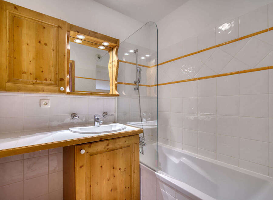 This charming bathroom features a wooden vanity with ample storage and a built-in mirror with integrated lighting.