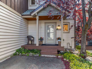 Charming entrance to a home featuring a covered porch with a brown chair and potted plants.
