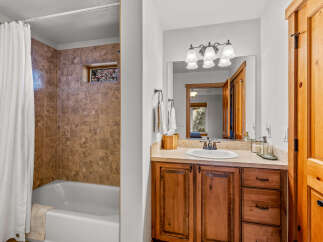 This bathroom features a tiled shower-tub combo with a white curtain and a small window offering a glimpse of nature.