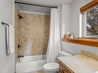 This bathroom features a tiled shower-tub combo with a white curtain, complemented by a white toilet and a vanity with a light-colored countertop.