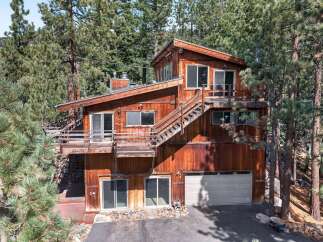 Nestled amidst tall pine trees, this multi-level wooden home offers a unique architectural design with expansive decks and an inviting exterior.