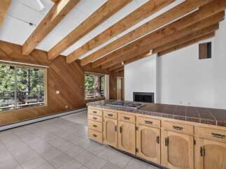 Experience rustic charm in this spacious living area featuring a vaulted ceiling with exposed wooden beams and a cozy fireplace.