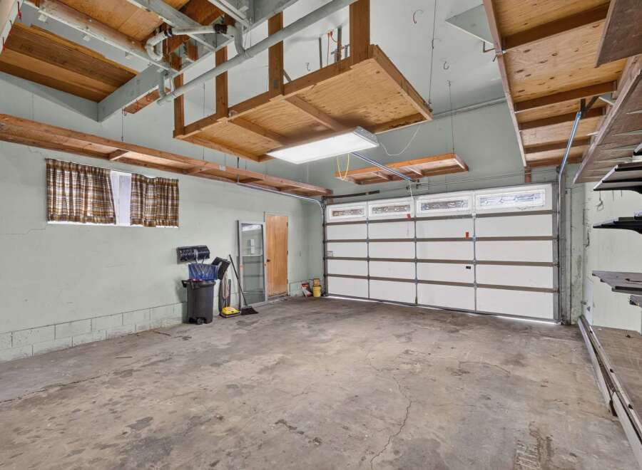 This spacious garage offers ample storage solutions with overhead wooden shelves and wall-mounted shelving units.