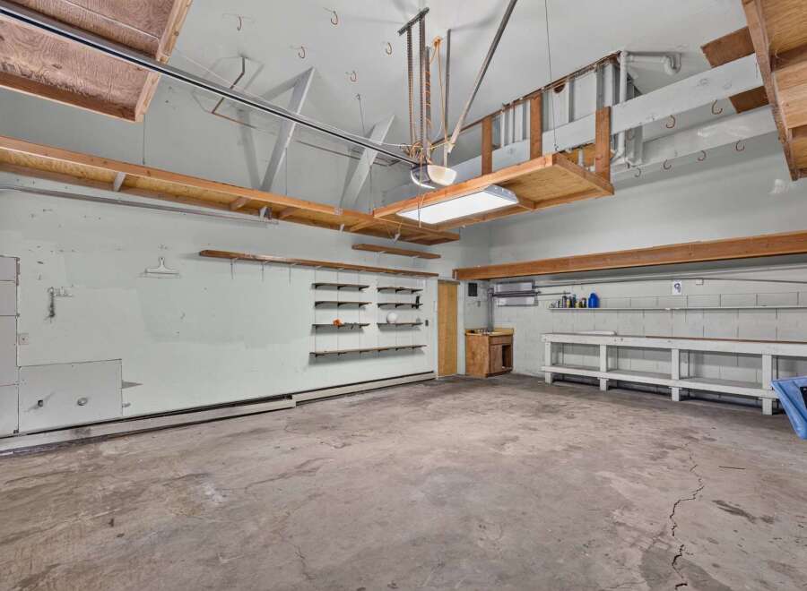 Discover ample storage and workspace in this spacious garage, featuring multiple shelves and a large workbench.