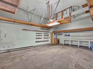 Discover ample storage and workspace in this spacious garage, featuring multiple shelves and a large workbench.