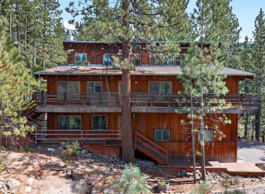 Nestled amidst towering pine trees, this multi-level wooden home offers a rustic retreat with ample outdoor living space.