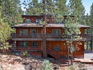 Nestled amidst towering pine trees, this multi-level wooden home offers a rustic retreat with ample outdoor living space.